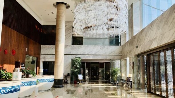 Un'ampia hall con pavimento in marmo, un grande lampadario e una reception con sedute a righe bianche e blu.