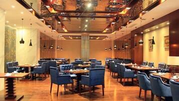 A spacious dining area with multiple tables and chairs, a high ceiling with intricate designs, and pendant lighting.