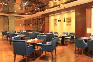 A restaurant with multiple dining tables and chairs, wooden flooring, and pendant lighting.