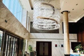 Um hall de entrada com um grande candelabro, colunas de mármore e um balcão de recepção.