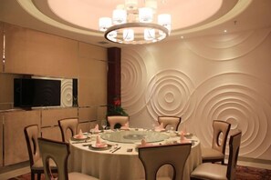Une salle de conférence avec une table ronde, des chaises, un lustre et un téléviseur fixé au mur.