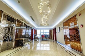 A hotel lobby with a polished floor, a seating area with a sofa, and a large window providing natural light.