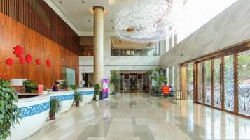 A spacious lobby with a reception desk, large chandelier, and a high ceiling.