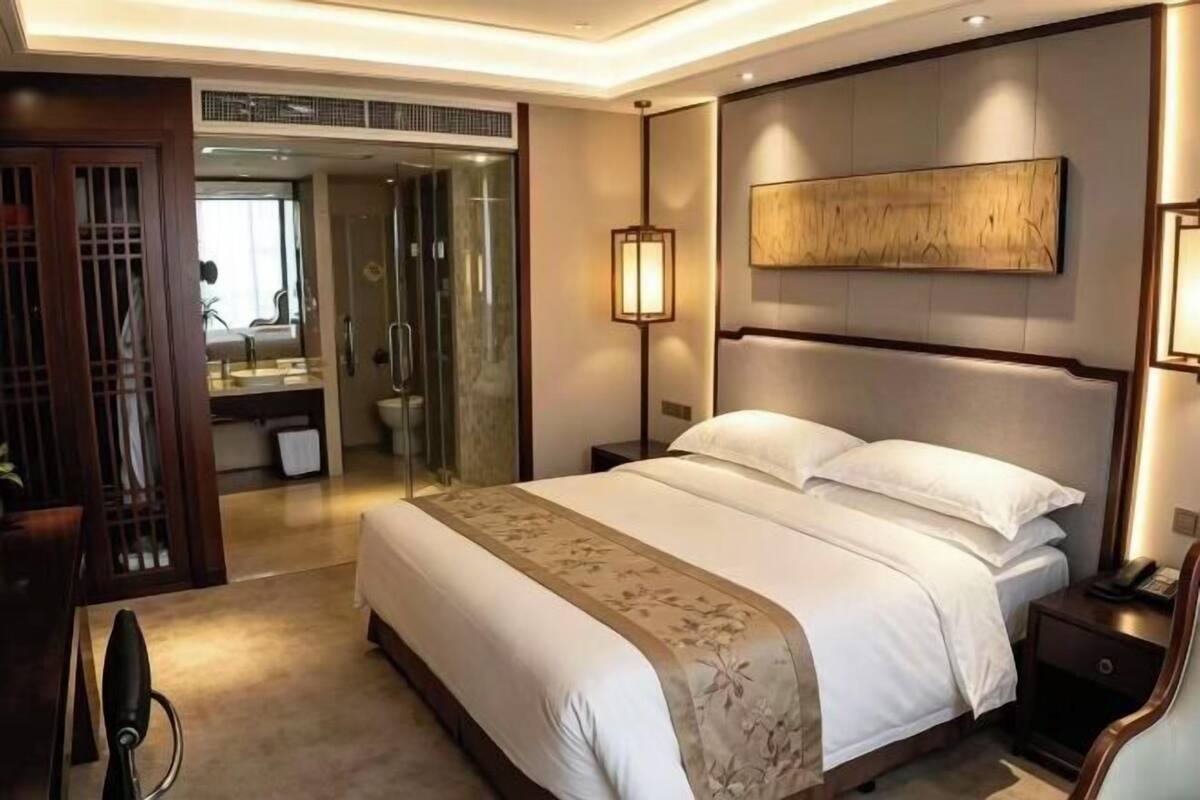 Ein Hotelzimmer mit einem großen Bett, Nachttischen, einem Spiegel, einem Kleiderschrank und einem durchgegangenen Tür erkennbaren Badezimmer.