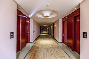 Corredor de hotel com portas de madeira, piso estampado e luminária no teto.