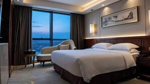 A hotel room with a large bed, a chair, a small table, and a city view through large windows. - Wuxi Yuexi Grand Hotel (Huishan Wanda) (Wuxi)