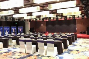 A conference room with rows of chairs, a stage, and a large screen.