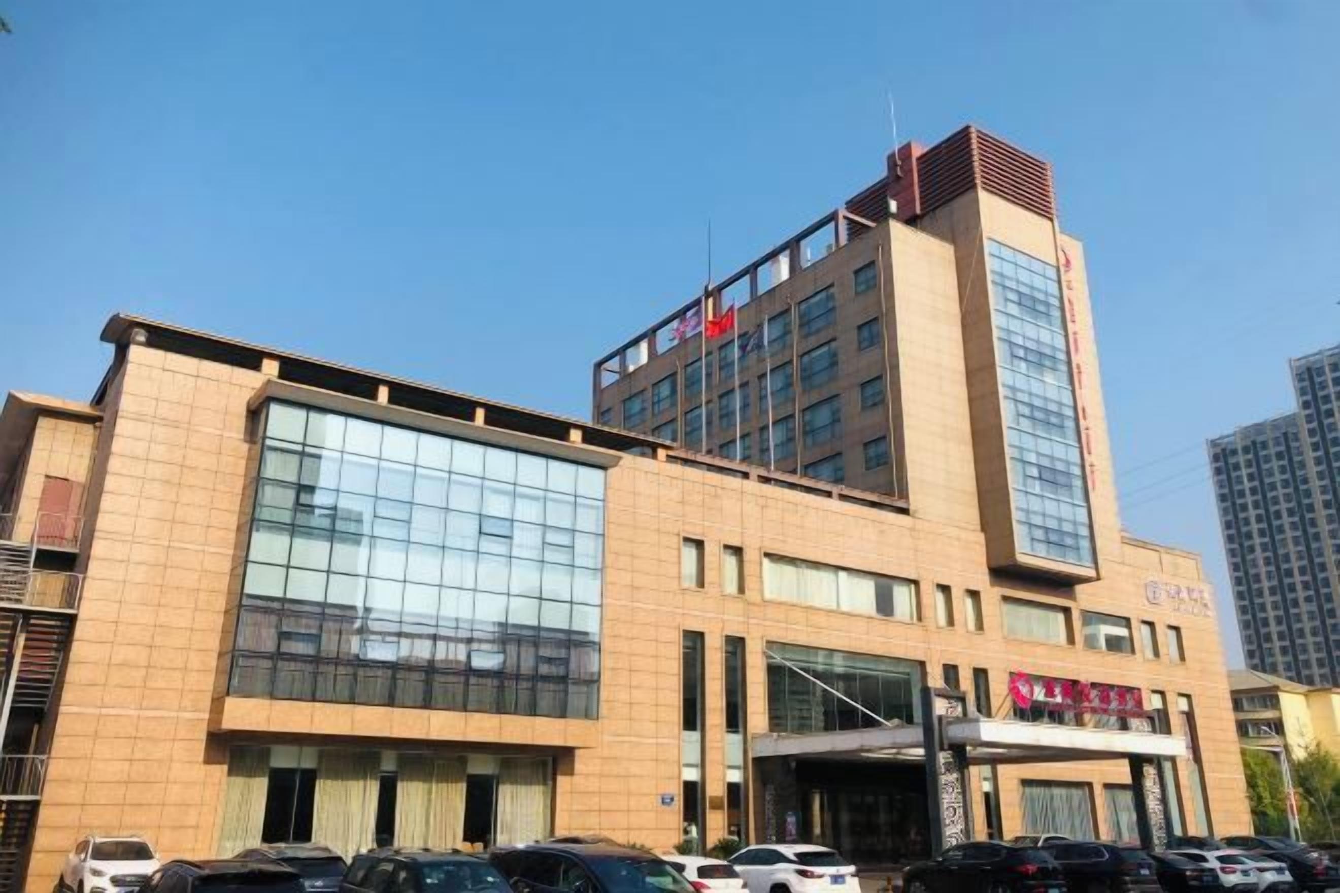 Un edificio de varios pisos con una fachada de vidrio destacada, una bandera en la cima y un letrero con caracteres chinos.
