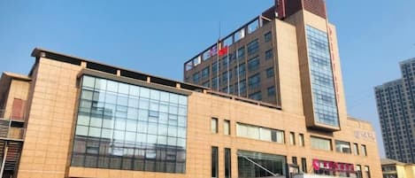 A multi-story building with a prominent glass facade, a flag on top, and a sign with Chinese characters.