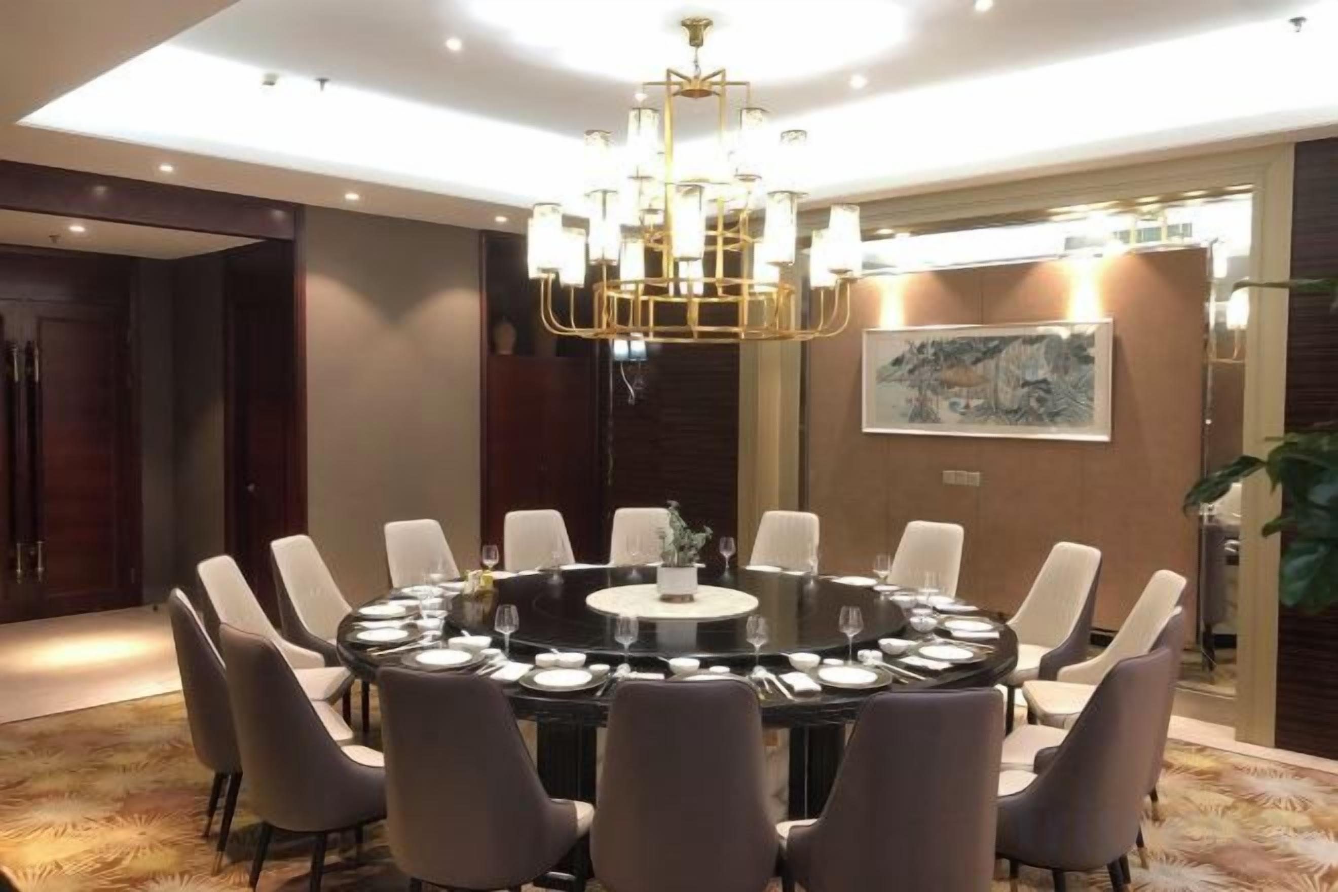 Une table de salle à manger ronde, entourée de chaises, un lustre et un tableau accroché au mur.