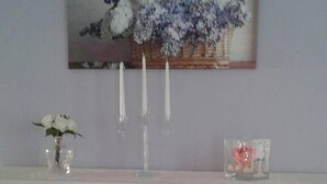Un meuble blanc avec des portes en verre, un vase rempli de fleurs blanches et un tableau représentant des fleurs violettes accroché au mur.