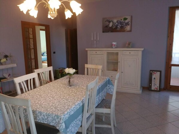 A dining area with a table set for four, surrounded by white chairs. A vase with flowers is on the table. There is a cabinet with glass doors and a painting above it. - Casa Annick Holiday Home Chianti Area Florence (Barberino Tavarnelle)
