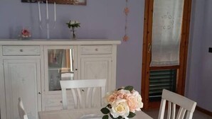 Un coin repas avec une table et des chaises blanches, un vase rempli de fleurs et un lustre.