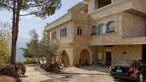 A large, multi-story building with a stone facade, arched windows, and a car parked in front. - Maison de la Vallee Private Guest House Great View (Kahlouniyeh)