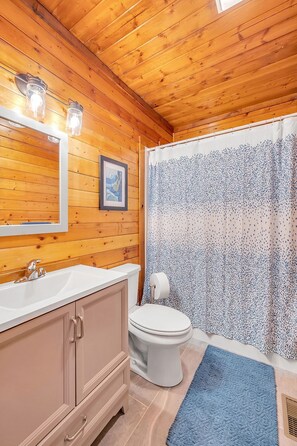 Ein Badezimmer mit Holzwandverkleidung, das ein Waschbecken, einen Spiegel, eine Toilette und eine Duschvorhang umfasst.
