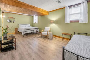 Ein Zimmer mit einem Bett, einem Sessel, einer Lampe, einem kleinen Tisch und einem Spiegel an der Wand.