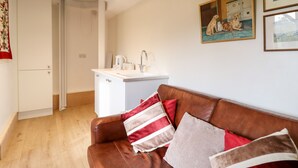 Una sala de estar moderna con un sofá de cuero marrón, una kitchenette blanca y un cuadro de perros en la pared.