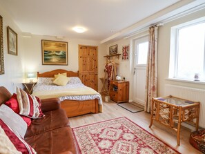 Um quarto aconchegante com cama, guarda-roupa de madeira, uma mesinha e uma janela com cortinas.