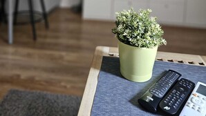 A living room with a potted plant on a table, two remote controls, and a modern kitchen in the background. - Charming 1-bed Apartment in Zagreb (Zagreb)