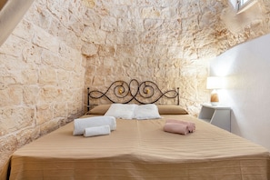 A bedroom with a stone wall, a metal bed frame, and a bedside table with a lamp.
