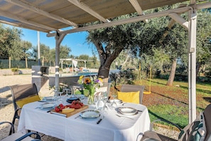 An outdoor dining area with a table set for two, surrounded by chairs, a pergola, and a view of a pool and trees. - Trullo Delle Ginestre Private Pool (Latiano)