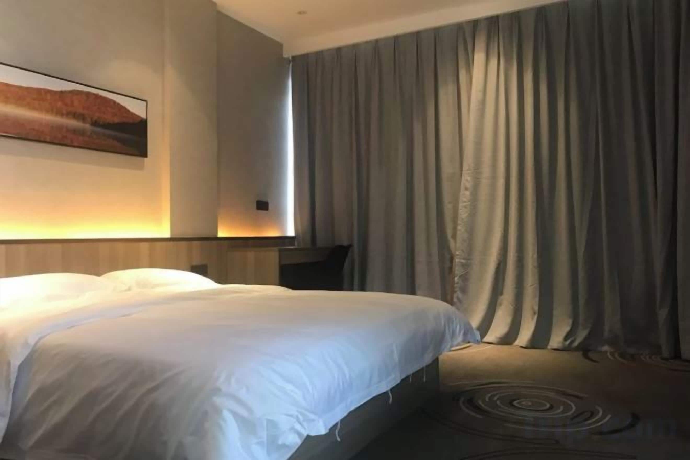 Ein Hotelzimmer mit einem großen Bett, einem Wand-Fernseher und einem Fenster mit Vorhängen.