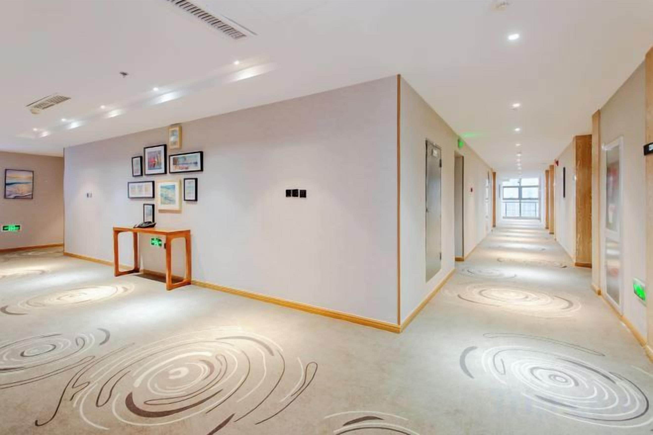 Un pasillo de hotel con piso alfombrado, cuadros en las paredes y una mesa de madera.