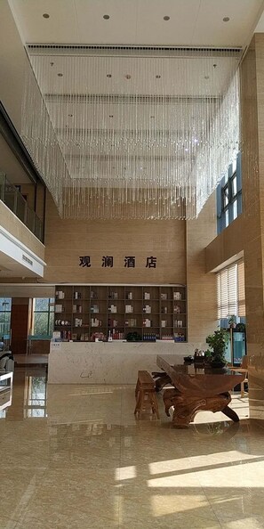A hotel lobby with a high ceiling, a wooden reception desk, and a large bookshelf.