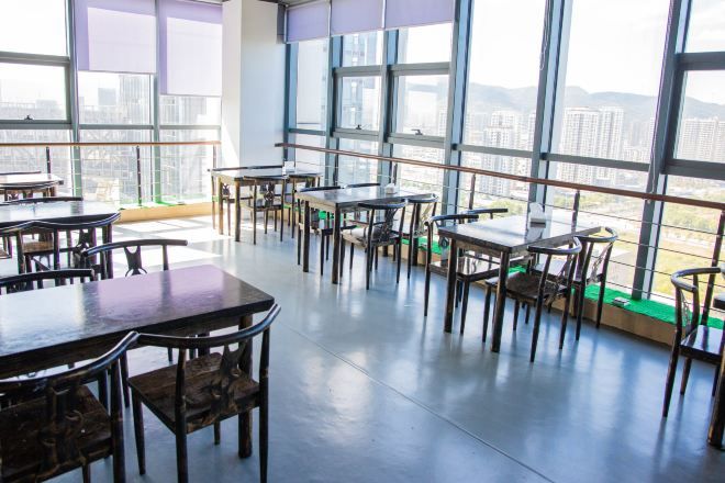 Un amplio espacio interior con mesas y sillas dispuestas para comer, grandes ventanales con vistas a la ciudad y un techo alto.