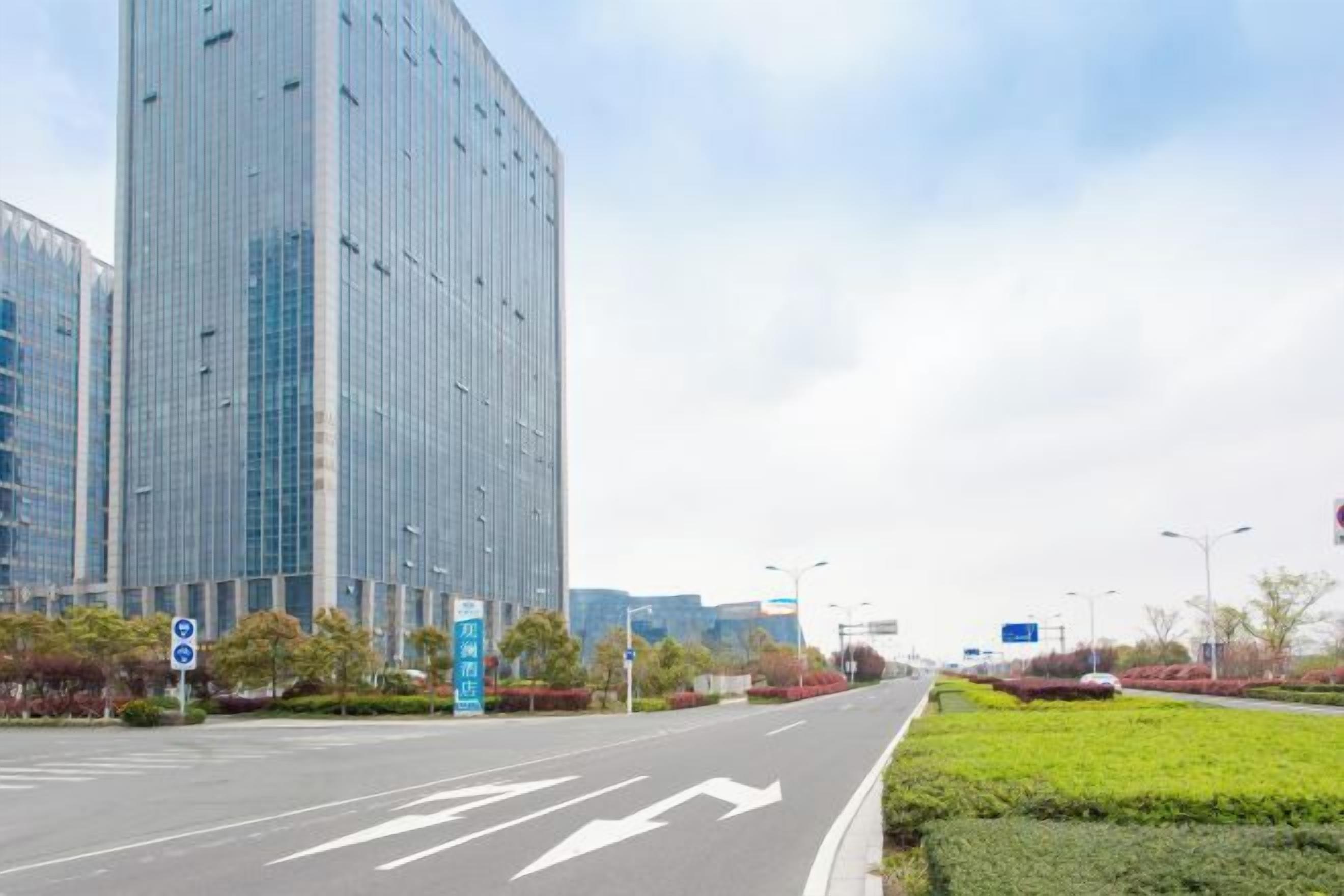 Une large route avec des flèches indiquant la direction, un bâtiment moderne et un ciel dégagé.