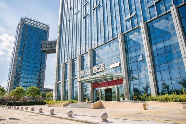 A modern building with a glass facade, a prominent entrance with a red awning, and a clear sky.