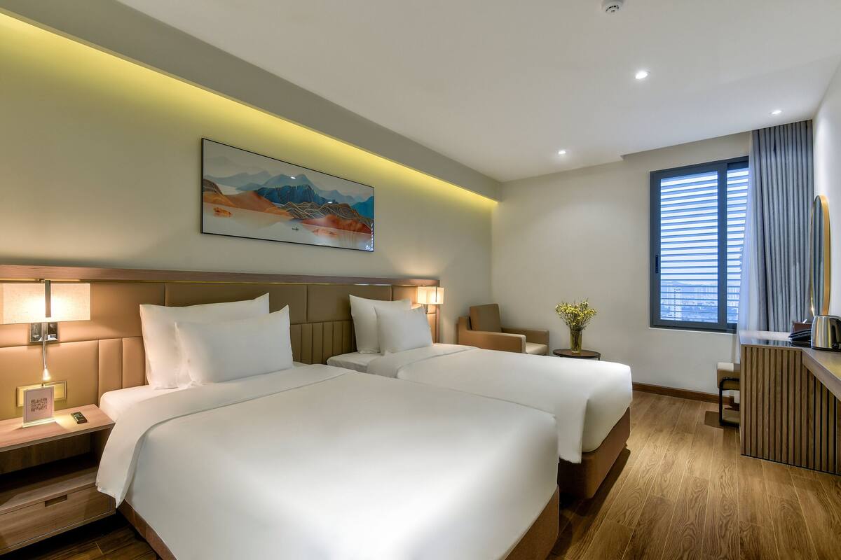 Una habitación de hotel con dos camas, un escritorio, una silla, una ventana con persianas y un cuadro en la pared.
