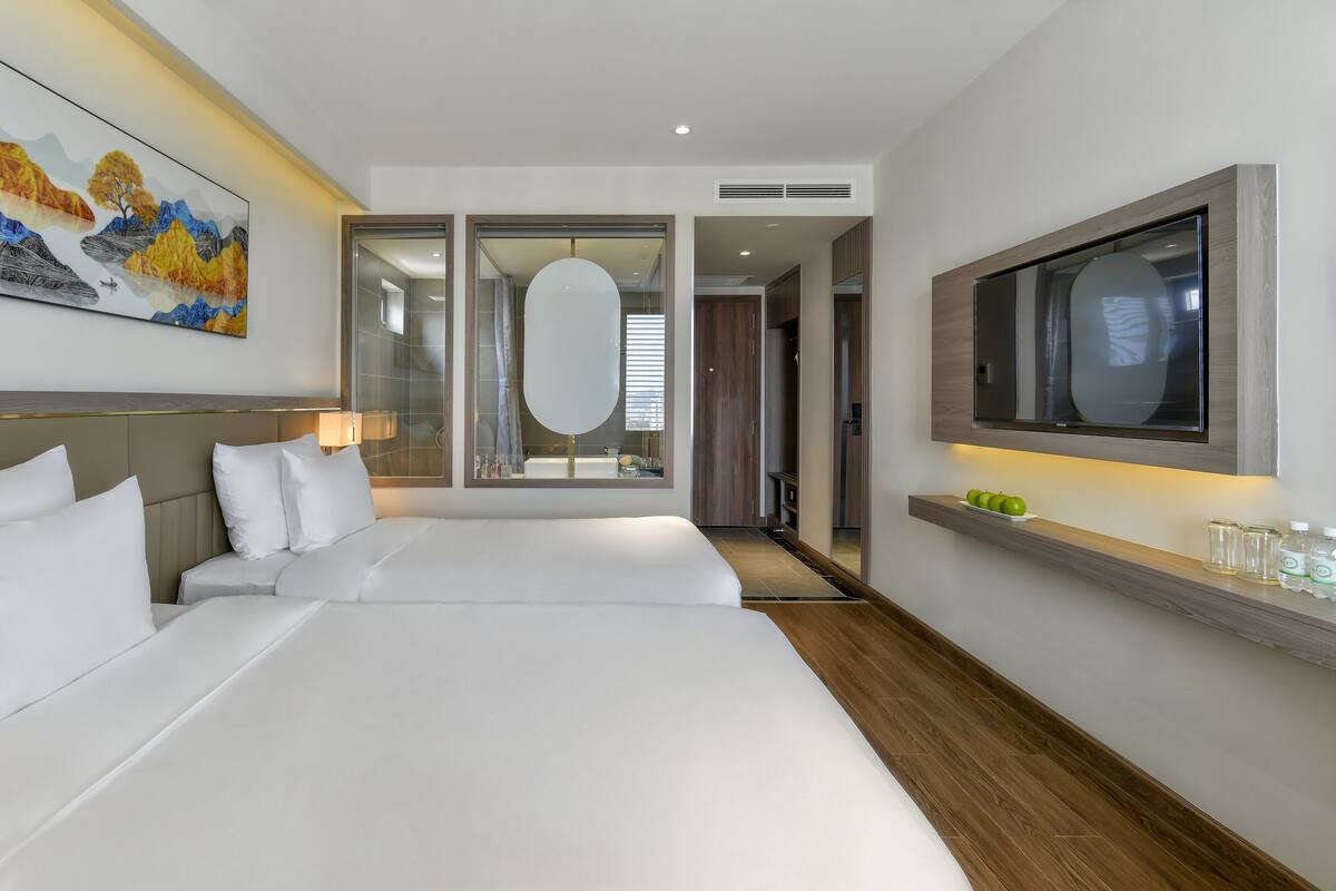 Una habitación de hotel moderna con una cama grande, un televisor montado en la pared y un cuadro sobre la cama.