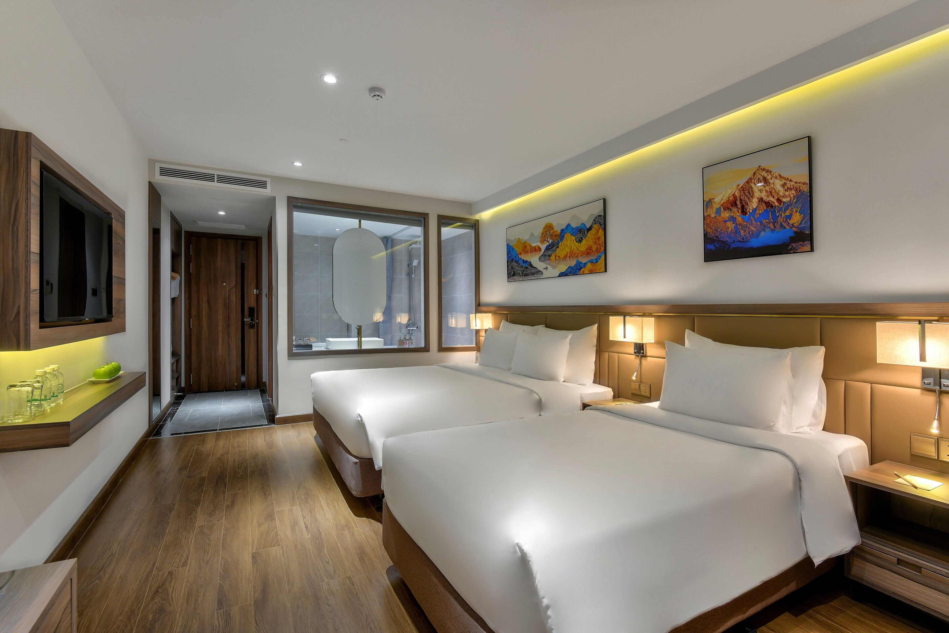 Habitación de hotel con dos camas, un baño con un espejo grande y un cuadro en la pared.