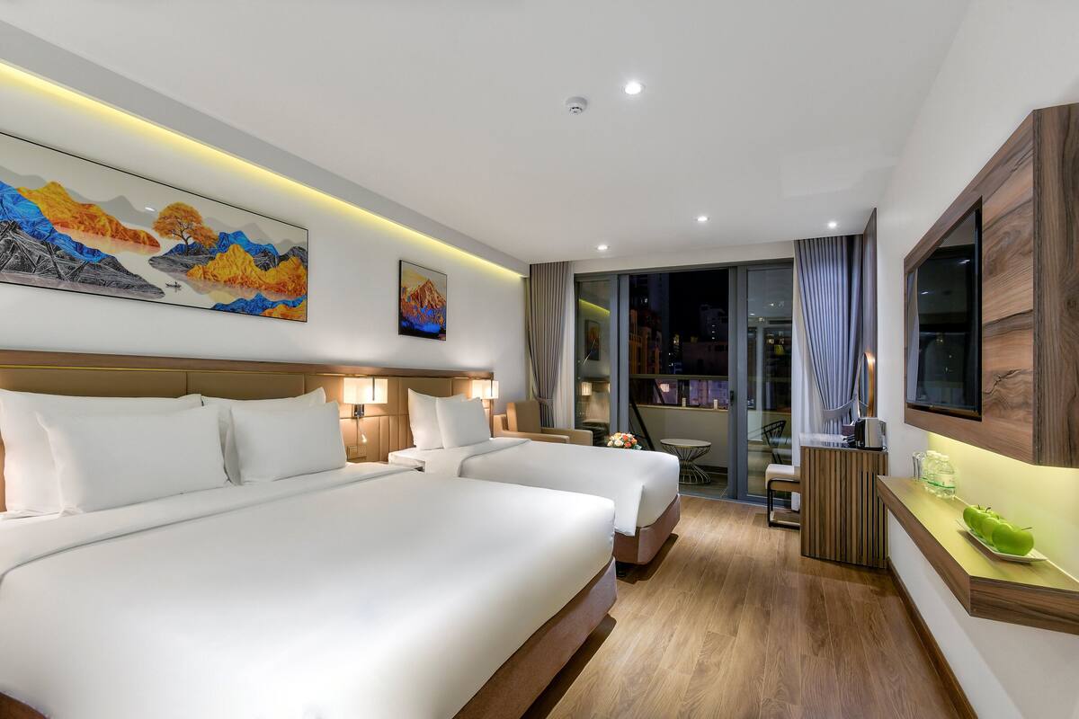 Habitación de hotel con dos camas, un escritorio, una silla, un televisor y obras de arte en las paredes.