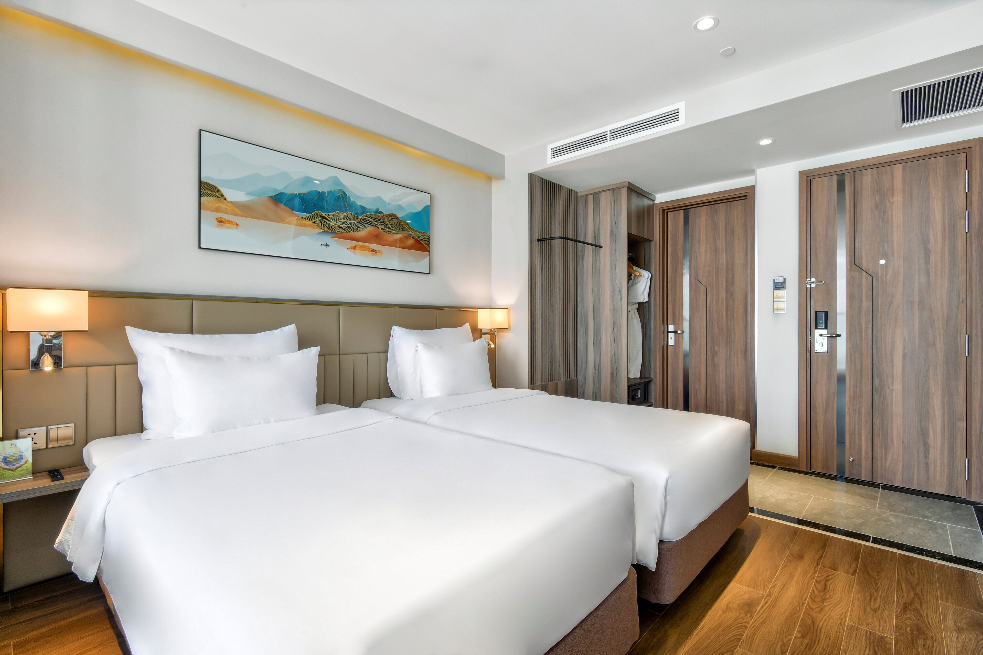 A hotel room with two beds, a painting on the wall, and wooden wardrobes.
