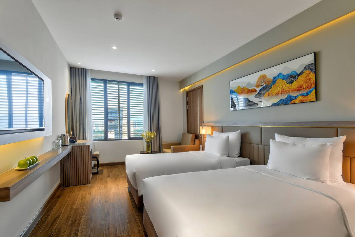 Habitación de hotel con dos camas, un escritorio de madera, un cuadro y una ventana con cortinas.