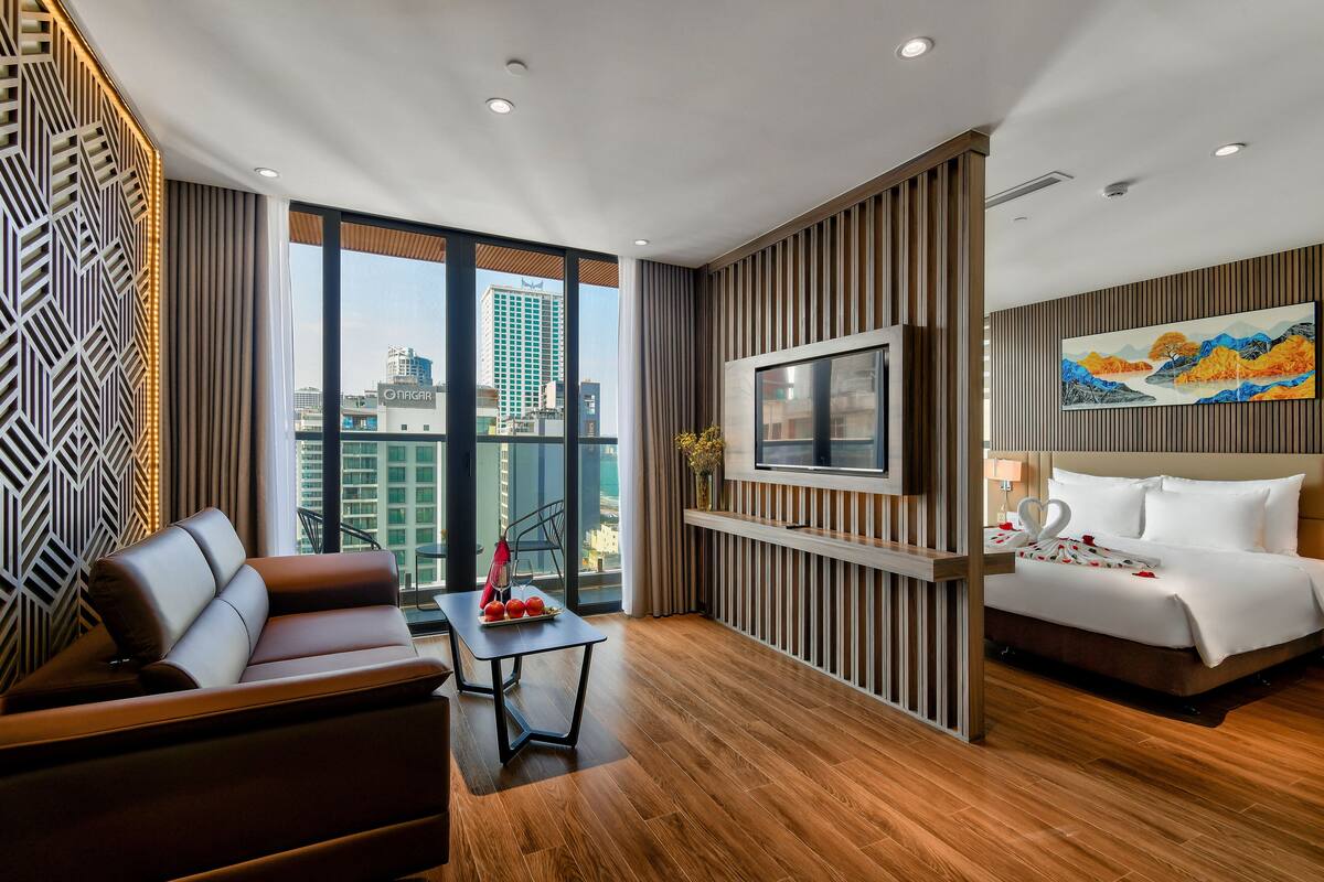 Una habitación de hotel moderna con un ventanal grande, un sofá, una cama y un televisor de pantalla plana.