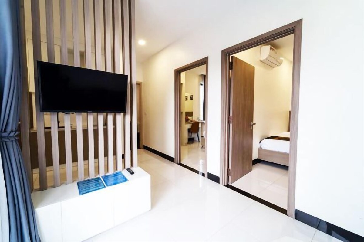 Une chambre d’hôtel moderne avec un téléviseur à écran plat fixé au mur, une cloison en lattes de bois et une petite table blanche sur laquelle se trouve un objet bleu.