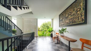 Un interior moderno con una escalera, piso a cuadros, un balcón con vegetación y un gran elemento decorativo en la pared.