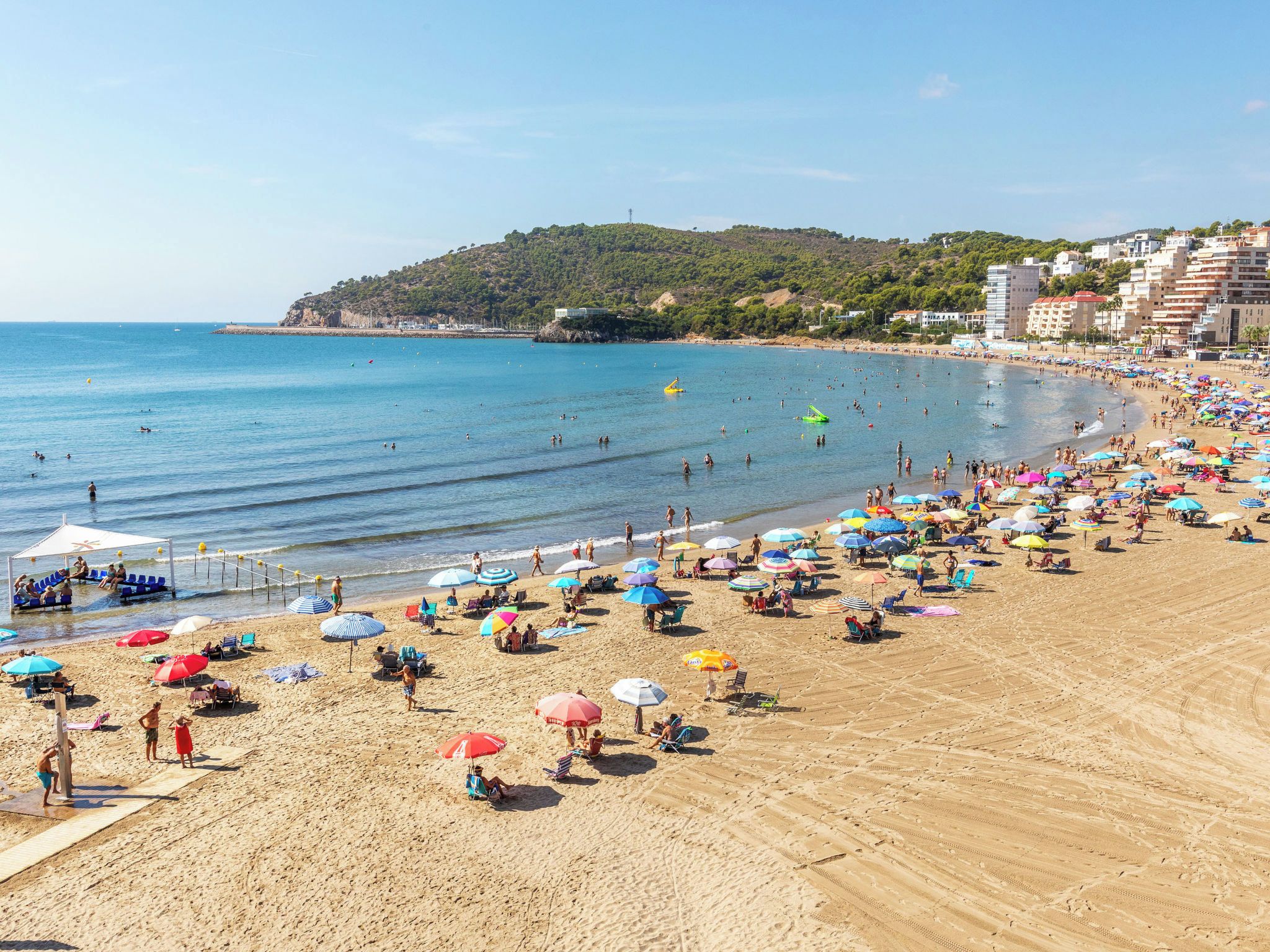 Une plage avec de nombreux parasols, des chaises longues et des gens qui profitent de la mer.