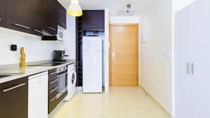 Une cuisine moderne avec des meubles de couleur sombre, un four à micro-ondes, un lave-linge et une porte en bois donnant sur une autre pièce.