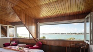 Camera da letto con un'ampia finestra vista su un corpo d'acqua, un letto, un tavolino e due sedie.