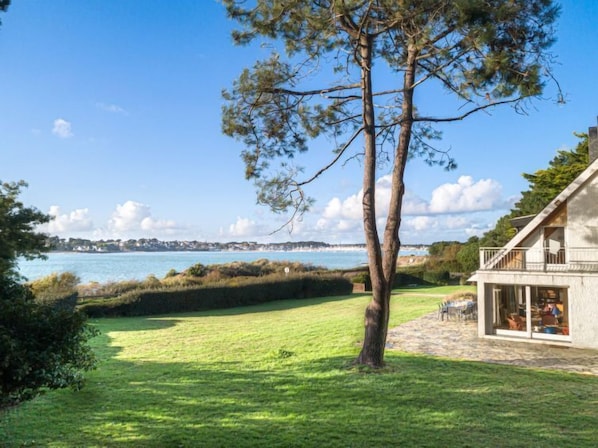 Une propriété située sur la côte, dotée d’une pelouse verdoyante, d’un arbre et d’un bâtiment avec un balcon donnant sur la mer.