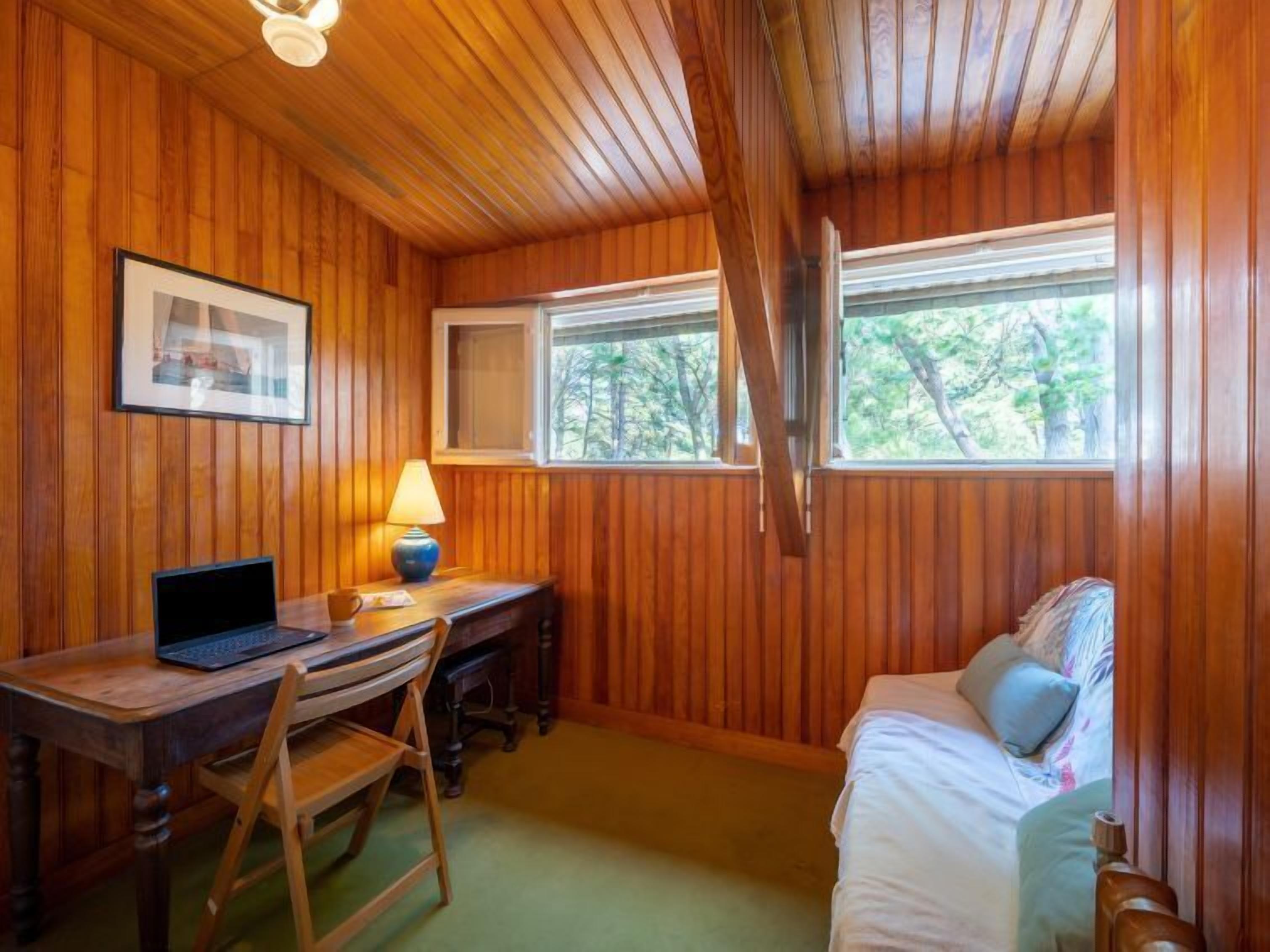 Une pièce aux murs lambrés, avec un bureau, une chaise et un lit.