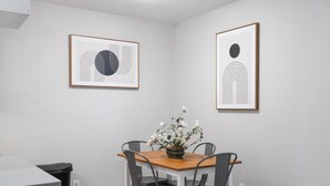 A dining area with a wooden table and four chairs, a vase with flowers, and two framed abstract artworks on the walls. - Stylish 1BR Near UT Highland Evonify (Austin)