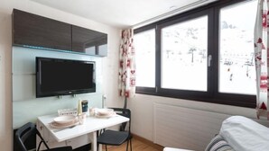 Ein kleines Zimmer mit Küchenzeile, einer Essecke und einem großen Fenster mit Blick auf eine verschneite Landschaft.