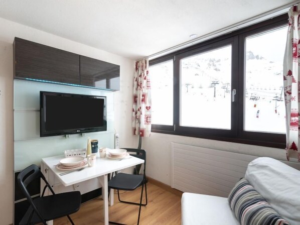 A compact room with a kitchenette, a dining area, and a large window with a view of a snowy landscape.