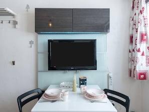 A dining area with a table set for two, a flat-screen TV mounted above, and a decorative wall with a Christmas tree ornament.