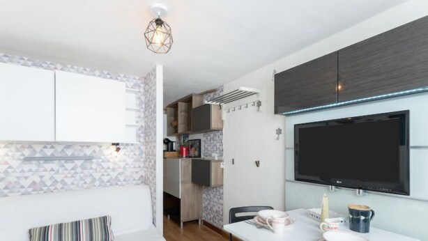 Eine moderne Küche mit integriertem Fernseher, ein Essbereich mit weißem Tisch und Stühlen und eine gemütliche Sitzecke mit gestreiftem Kissen.
